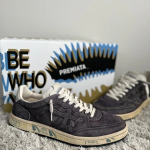 Premiata skor - Snygga sneakers från Premiata i mörkgrå/blå mocka med vita detaljer och snörning färgen på skorna heter ”clay” men är som mörkblå eller grå. Skorna har en beige-vit sula med tryck och mörkblå/grå yttersula. Skorna är storlek 41 skulle nog passa 40 också. Perfekta för vintern om du vill vara stillren. Box ingår!