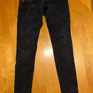 Svarta Replay jeans Anbass 32/32 - Svarta Replay Anbass jeans i storlek 32/32. Modellen har en slim passform med raka ben och klassiska fem fickor. Jeansen är tillverkade i mjukt denimtyg med diskreta sömmar och Replay-logga på insidan. Perfekt för dig som gillar stilrena och moderna jeans.