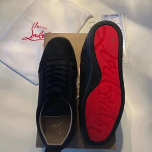 Svarta Christian Louboutin skor - Snygga svarta sneakers från Christian Louboutin med klassisk rund tå och platt sula. Skorna har svart ovandel i skinn och signifikant röd sula med Louboutin-logga. Kommer med dustbag och originalkartong. Perfekt för dig som gillar exklusiv streetstyle. Kvitton ingår.
