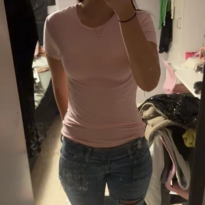 Ljusrosa tight kortärmad topp - Säljer en ljusrosa topp med tight passform och korta ärmar. Enkel och stilren design, perfekt att matcha med jeans eller kjol. Mjuk och skön mot huden, passar dig som gillar en clean look.