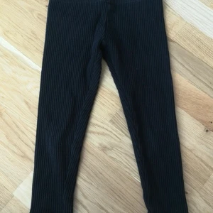 Svarta ribbade leggings från H&M - Svarta ribbade leggings från H&M i storlek 98. De är stretchiga och mjuka med en smal passform och elastisk midja. Aldrig blivit använda, så är som nya.