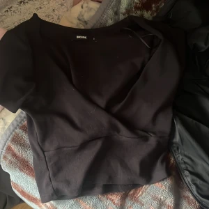 Svart omlottopp från Bik Bok - Säljer en svart omlottopp från Bik Bok i storlek S. Toppen har korta ärmar och en snygg omlottdesign som ger en cool och modern look. Materialet är mjukt och känns skönt mot huden. Perfekt att styla med jeans eller kjol för en trendig vibe.