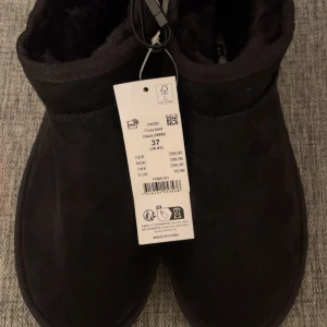 Svarta cozy boots i mocka, stl 37 - Mysiga svarta boots i mocka med mjukt foder och platt sula. Perfekta för kalla dagar med sin enkla och stilrena design. Skorna har rund tå och låg profil, vilket gör dem både snygga och bekväma att bära. Helt nya 