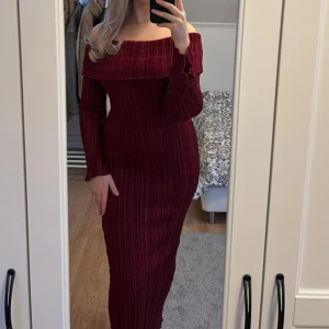 Vinröd offshoulder långklänning - Säljer en vinröd långklänning med offshoulder och ribbad struktur. Klänningen har långa ärmar och sitter tight mot kroppen. Använd endast en gång!