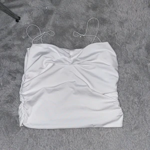 Vit omlott linnetopp från Amisu - Säljer en vit linnetopp från Amisu i storlek L (men passar en S/M/L). Toppen har tunna axelband, snygg omlott-effekt och rynkade sidor som ger en cool look. Materialet är mjukt och har lite glans, perfekt för att lyfta din outfit. Passar dig som gillar stilrena och trendiga plagg.