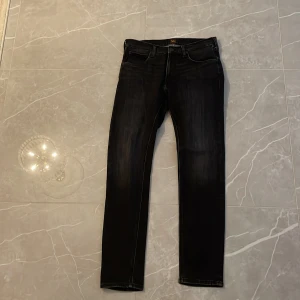 Svarta jeans från Lee - Snygga svarta jeans från Lee med skinny passform och klassisk femficksdesign. Jeansen har en mörk tvätt med subtila slitningar och Lee-logga på bakfickan. Perfekt för dig som gillar en smal siluett och stilren look.