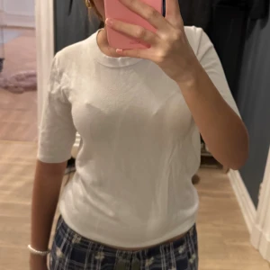 Vit stickad tröja med ribbade detaljer - Säljer en enkel och stilren vit stickad tröja med ribbade muddar vid ärmslut och nederkant. Tröjan har korta ärmar och rund halsringning, perfekt för en clean och fräsch look. Passar till allt och är superenkel att styla.