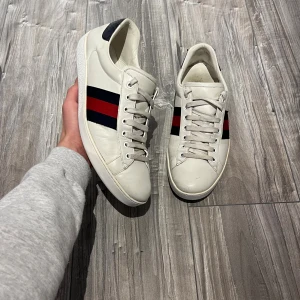 Gucci Ace vita sneakers med röd och blå rand - Riktigt snygga Gucci ace skor i strl 43. Väldigt fint skick, riktigt fräscha förutom lite slitningar på insidan av skon som man inte ens ser. Hör av dig vid frågor.