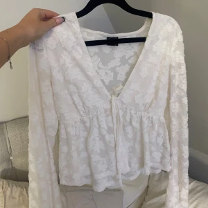 Vit blommig blus med knyt - Säljer en superfin vit blus med blommigt mönster och transparenta partier. Blusen har v-ringning, långa ärmar och en söt knytning framtill. Materialet känns lätt och luftigt, perfekt för vår och sommar. Passformen är normal och volangen nedtill ger en extra touch. Använd 1 gång och köptes för 299