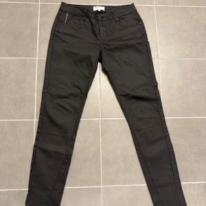 Svarta jeans från Pulz, strl 38 - Svarta jeans från Pulz i modellen Jamee. Byxorna har dragkedjor på bakfickorna och klassisk femficksdesign. Materialet är en mix av bomull, polyester och elastan för skön stretch. Snygg passform som sitter tight hela vägen ner.