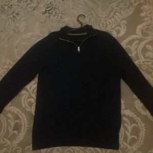 Mörkblå stickad tröja med half zip - Mörkblå stickad tröja i storlek M med halv dragkedja vid halsen. Tröjan har lång ärm och en klassisk, enkel design som passar perfekt till lager-på-lager-stil under höst och vinter. Snygg och stilren att matcha med jeans eller chinos.