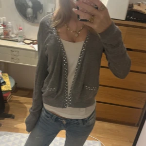 Grå kofta med pärldetaljer från H&M - Grå kofta från H&M med snygga pärldetaljer längs kanterna och på fickorna. Modellen är croppad och har lång ärm, perfekt att slänga över ett linne eller t-shirt. Mjuk och tunn stickad känsla som funkar året runt. Skulle säga att den är ganska liten så kanske S ist för M❤️