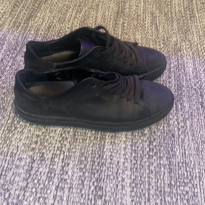 Svarta sneakers från Axel Arigato - Säljer ett par svarta sneakers från Axel Arigato med stilren design och rund tå. Skorna har snörning och är tillverkade i skinn med platt sula. Perfekta för dig som gillar minimalistisk och clean stil.