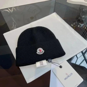 Svart ribbad Moncler mössa - Svart ribbstickad mössa från Moncler med klassisk uppvikt kant och ikonisk logotyp framtill. Perfekt accessoar för kyliga dagar, tillverkad i mjukt material som sitter skönt på huvudet.