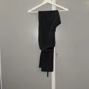 Gråa byxor från Fashion Nova - Snygga grå byxor från Fashion Nova med elastisk midja och slits vid benslut. Materialet är mjukt och stretchigt syntet, vilket gör dem bekväma och följsamma. Perfekt för dig som gillar en trendig och stilren look.