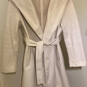 Beige kappa - Snygg beige kappa från Zara med stor huva och knytskärp i midjan. Använd ett fåtal gånger, kan vara något nopprig under armen men inget som syns!