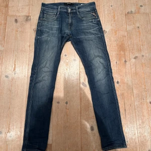 Replay Anbass jeans i mörkblå denim - Snygga Replay Anbass jeans i mörkblå tvätt med slitningar och klassiska fem fickor. Jeansen har smal passform, normal midja och detaljerade bakfickor med Replay-logga. Perfekta för dig som gillar en modern och stilren look.