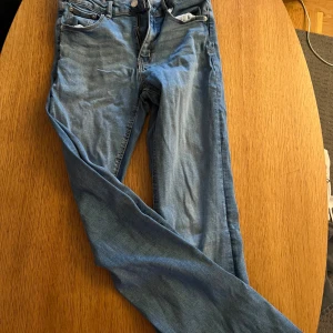 Blå jeans från Gina Tricot, storlek 158 - Snygga blå jeans från Gina Tricot i storlek 158. Klassisk femficksmodell med raka ben och coola bakfickor med lock och knapp. Jeansen har normal passform och är tillverkade i mjukt denimtyg som sitter skönt hela dagen.