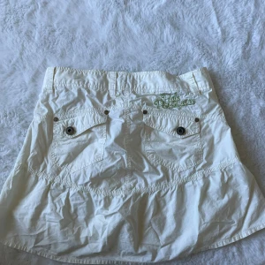 Vit cargokjol från Peak Performance - Säljer en vit cargokjol från Peak Performance med coola fickor bak och broderad logga i grönt. Storlek S💕den har små fläckar där framme men går säkert bort i tvätten