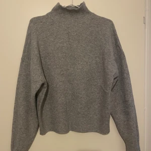 Grå polotröja från Gina Tricot - Grå polotröja från Gina Tricot i stickat material. Tröjan har hög krage, lång ärm. Har mudd nertill och på armarna. 