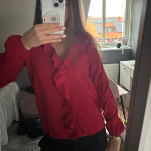 Röd volangblus från Vero Moda XS - Supersnygg röd blus från Vero Moda i storlek XS. Skjortan har långa ärmar, v-ringning och en cool volangdetalj framtill. 