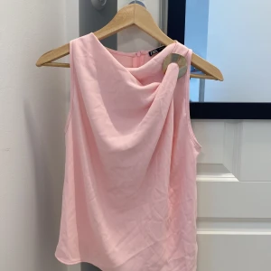 Ljusrosa ärmlös topp från Zara - Säljer en jätte gullig ljusrosa ärmlös topp från Zara med snygg drapering framtill och rund hals. Toppen har en mjuk, slät yta och stängs med dragkedja i ryggen. Endast använd en gång