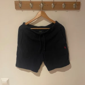 Svarta shorts från Polo Ralph Lauren - Svarta shorts från Polo Ralph Lauren med klassisk röd logga broderad på benet. Mjukt material, dragsko i midjan och två fickor framtill. Perfekta för chill dagar eller när du vill ha en clean och enkel stil.