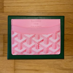 Rosa Goy4rd plånbok - Supersnygg rosa plånbok från Goy4rd med deras ikoniska grafiska mönster i ljusrosa och vitt. Plånboken har flera kortfack och är tillverkad i skinn och canvas. Perfekt accessoar för dig som vill sticka ut med något unikt och lyxigt.