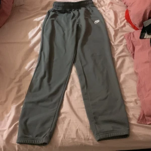 Grå mjukisbyxor från Nike XL - Grå mjukisbyxor från Nike i storlek XL, med elastisk midja och klassisk vit Nike-logga på vänster höft. Byxorna har raka ben och är tillverkade i mjukt material som passar perfekt för chill eller träning.