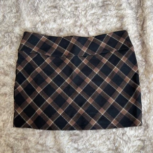 Rutig brun och svart minikjol från H&M - Supersnygg kort kjol från H&M med rutigt mönster i svart, brunt och beige. Kjolen har en rak passform och är tillverkad i en mjuk mix av viskos och polyester med lite stretch för extra komfort. 