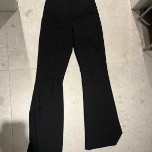 Svarta bootcut-byxor Gina Tricot XS - Snygga svarta bootcut-byxor från Gina Tricot i storlek XS. Byxorna har hög midja och raka pressveck längs benen som ger en clean och trendig look. Perfekta att styla med sneakers eller klackar för en cool vibe.