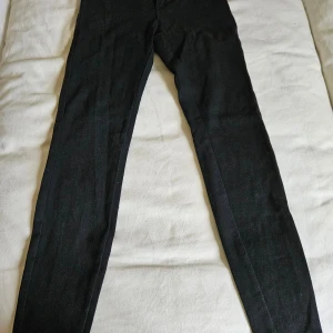 Svarta skinny byxor från Janina - Svarta byxor från Janina i storlek 36, med smal passform och klassisk skinny stil. Byxorna har en enkel design utan synliga detaljer och är gjorda i ett mjukt material som sitter tajt längs benen. Perfekta för dig som gillar en clean look.