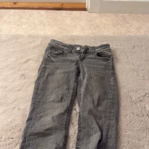 Grå jeans från Gina Tricot, storlek 146 - Snygga grå jeans från Gina Tricot i klassisk femficksmodell med knapp och dragkedja framtill. Jeansen har raka ben och en cool tvättad look. Bakfickan har lock med knapp. Perfekt för dig som gillar avslappnad stil.