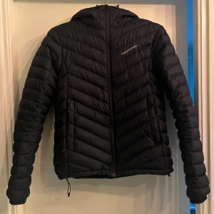 Marin blå dunjacka Peak Performance M - Marin blå dunjacka från Peak Performance i storlek M. Jackan har huva, dragkedja framtill och snygga diagonala quiltade sömmar. Perfekt för kyliga dagar och har en clean, sportig look. Passar dig som gillar stilren och funktionell design. Perfekt nu till vintern!