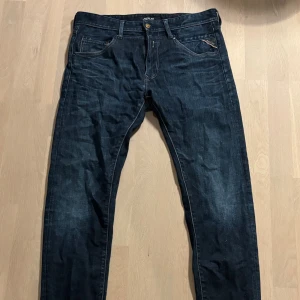 Mörkblå Replay jeans, modell MASIG - Snygga mörkblå jeans från Replay, modell MASIG. Klassisk femficksdesign med guldfärgad knapp och Replay-detalj på fickan. Jeansen har raka ben och är tillverkade i slitstarkt denimtyg. Perfekta för dig som gillar stilrena och tidlösa jeans.
