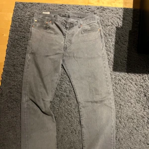 Grå Levi's 501 jeans W33 L34 - Säljer ett par grå Levi's 501 jeans med klassisk rak passform och knappgylf. Jeansen har fem fickor, silverfärgade nitar och den ikoniska läderpatchen bak. Perfekt för dig som vill ha ett par jeans som funkar till allt
