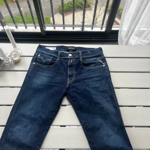 Mörkblå Replay jeans  - Snygga mörkblå jeans från Replay med klassisk femficksdesign . Slim fit med tydlig Replay-logga på bakfickan och vitt märke i linningen. Perfekta för en stilren och avslappnad look.