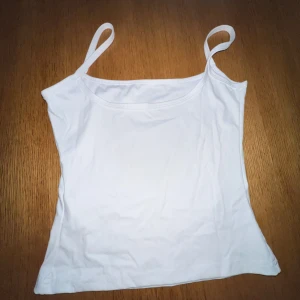 Vit linnetopp i polyamid XS - Säljer en enkel och fräsch vit linnetopp i storlek XS. Toppen har smala axelband och är figurnära med en mjuk, stretchig känsla tack vare materialet i polyamid och elastan. Perfekt för varma dagar eller som layering-piece.