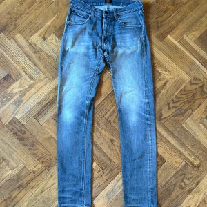 Blå/grå skinny jeans från Lee - Säljer ett par klassiska blå jeans från Lee med snyggt slitna detaljer och femficksmodell. Jeansen har smal passform och normal midja, tillverkade i mjukt denimtyg. Perfekta för dig som gillar en tidlös och avslappnad look.