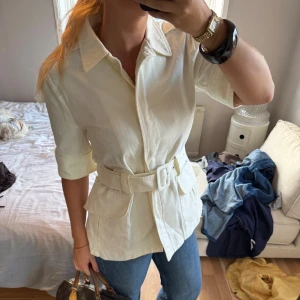 Vit skjorta med bälte och fickor❣️ - Snygg vit skjorta med krage och trekvartsärm, designad med ett matchande bälte i midjan och stora fickor framtill. Skjortan har en clean look och är gjord i mjukt bomullstyg som känns skönt mot huden. Perfekt för dig som gillar stilrena och trendiga plagg 