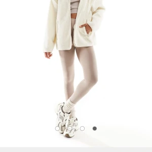 Vit teddyjacka med dragkedja - Mysig vit teddyjacka med dragkedja framtill och två fickor. Jackan har en avslappnad passform och är tillverkad i fluffigt fleece-material som ger en trendig look. Perfekt för lager-på-lager och passar till både jeans och tights.