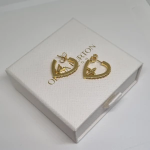 Guldörhängen med stenar  - Snygga örhängen i guld formade som hjärtan med små gnistrande stenar längs kanten. Varje örhänge har en söt liten bi-detalj inuti hjärtat. Perfekt för dig som gillar unika och glittriga accessoarer med en touch av natur. Lådan ingår ej.