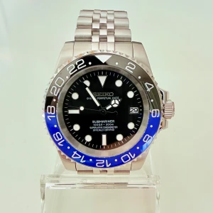 Seiko mod 40mm - Batman Submariner - Helt oanvänd Seiko Submariner mod med svart blå boett. Utrustad med Seikos NH35 urverk, med hållbart safirglas och en gridlock clasp, samma typ som används på en del rolexklockor som gör det lätt att justera klockans längd. DM mig om du vill ha fler bilder eller undrar något. Extra länkar följer också med. Pris är diskuterbart.