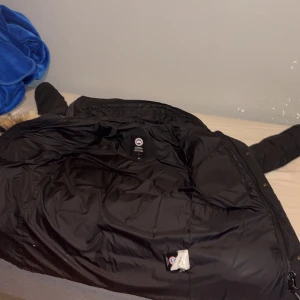 Svart dunjacka från Canada Goose M - Säljer en svart dunjacka från Canada Goose i storlek M. Jackan har huva med snygg pälsdetalj, långa ärmar och flera praktiska fickor framtill. Perfekt för kalla vinterdagar och har en klassisk, stilren look som funkar till allt. Pris kan alltid diskuteras pälsen är helt äkta och kvitto finns med.