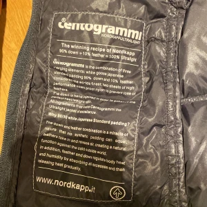 Svart lång dunjacka Nordkapp S - Svart, lång och quiltad dunjacka från Nordkapp Centogrammi Ultralight. Jackan har huva, dragkedja framtill och två sidofickor med dragkedja. Fylld med 90% dun och 10% fjäder, yttermaterial och foder i nylon. Perfekt för kalla dagar och har en clean, sportig look. Ny pris 2800kr