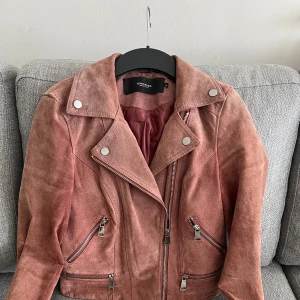 Rosa mockajacka från Vero Moda XS - Snygg rosa mockajacka från Vero Moda i storlek XS. Jackan har klassisk bikerstil med silvriga dragkedjor, bred krage och dekorativa knappar. Materialet är mjuk mocka och jackan är figursydd med långa ärmar och flera fickor med dragkedja.