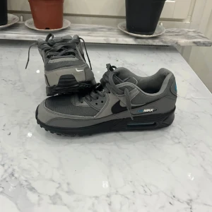 Nike Air Max 90 grå/blå sneakers - Säljer Nike Air Max med färg av grå, lite blått samt svarta sulor. Köpte de från JD men vill inte längre ha de, har haft på mig de ungefär 1-2 gånger. Kan tyvärr inte lämna tillbaka de på grund av att jag slängde iväg skokartongen :(