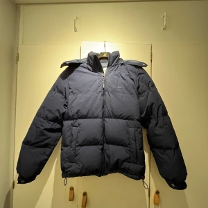 Mörkblå pufferjacka från Levi's XS - Säljer en mörkblå pufferjacka från Levi's i storlek XS. Jackan har huva, dragkedja framtill och två stora fickor. Perfekt för kalla dagar med sin vadderade design och justerbar nederkant. Klassisk och stilren look med diskret Levi's-logga. Köpt för 2000kr på NK man förra vintern. Tvättas innan frakt!