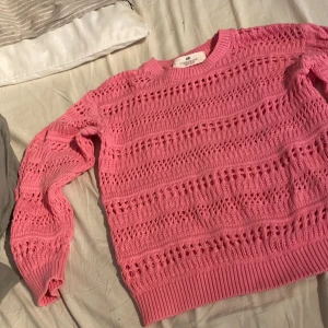 Rosa stickad tröja från H&M - Säljer en rosa stickad tröja från H&M med snyggt hålmönster och ribbade muddar vid hals, ärmslut och nederkant. Tröjan har långärmad passform och är gjord i mjuk bomull, perfekt för dig som gillar färg och detaljer.