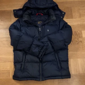 Dunjacka ifrån Ralph lauren - En stilren dunjacka från polo Ralph lauren i storlek 14-16 som motsvarar xs, passar perfekt till kyliga vinterdagar eller vardagsbruk, skicket är bra med inga synliga skador. original pris 3295 mitt pris 1499. Ps priset är prutbart vid en snabb och smidig affär. 